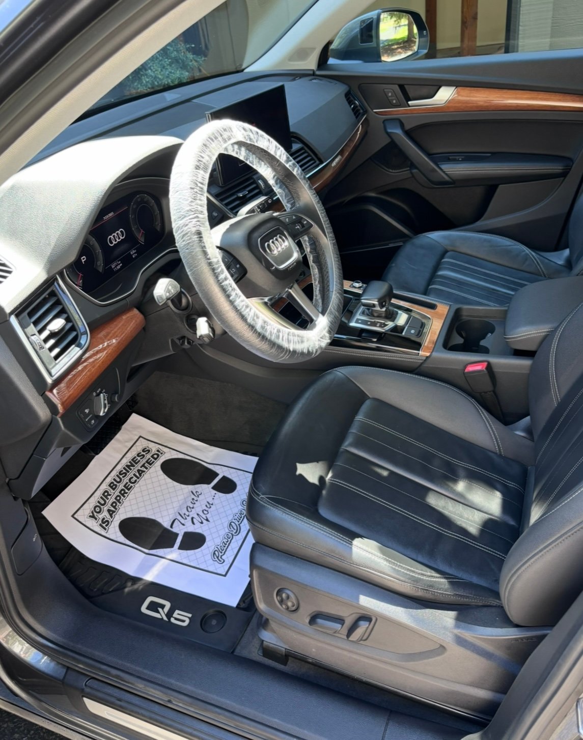Interior of an Audi Q5 with steering wheel cover, blue leather seats, wooden trim accents, and an instruction manual on the floor