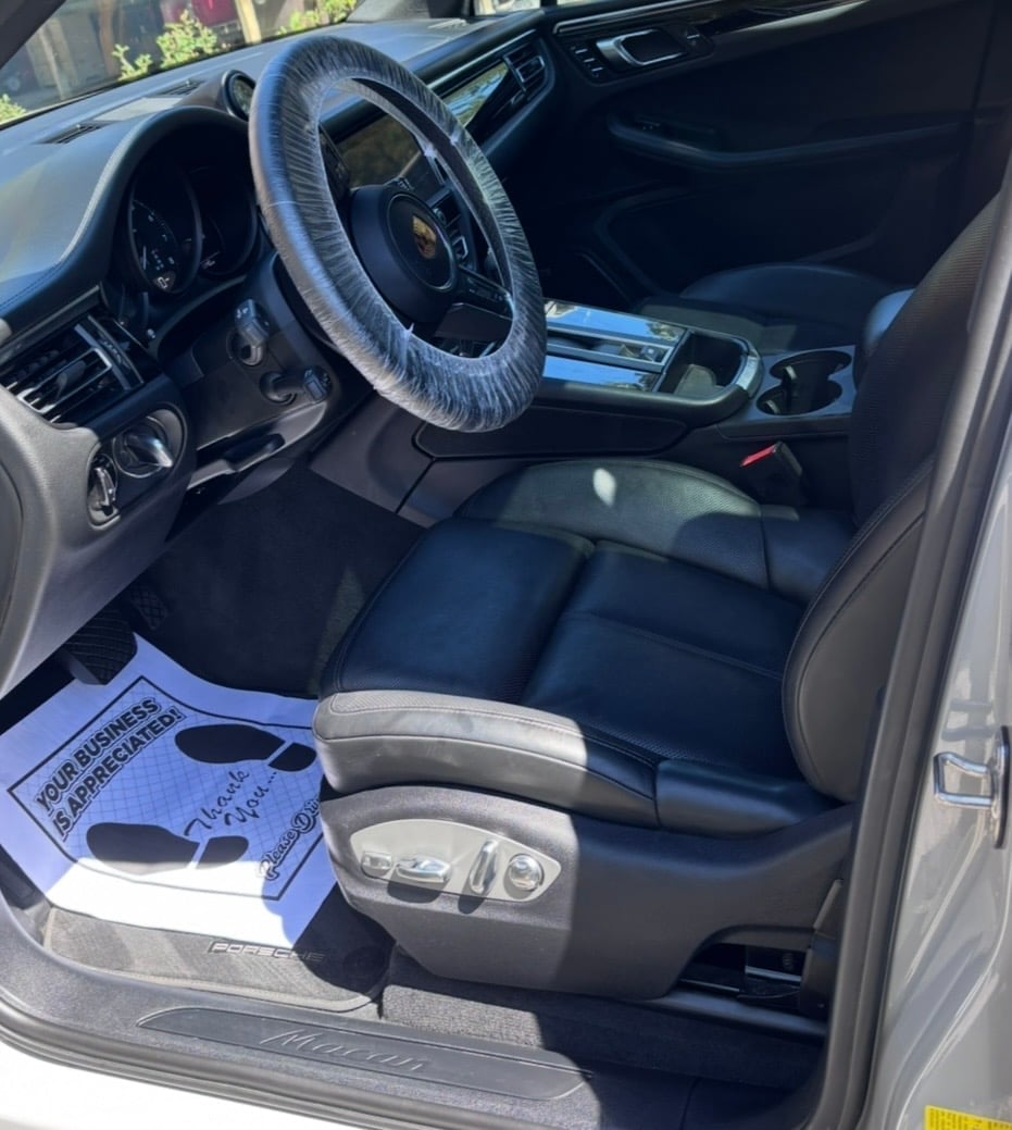 Car interior with blue steering wheel cover, black leather seats, and dashboard, door open showing paperwork